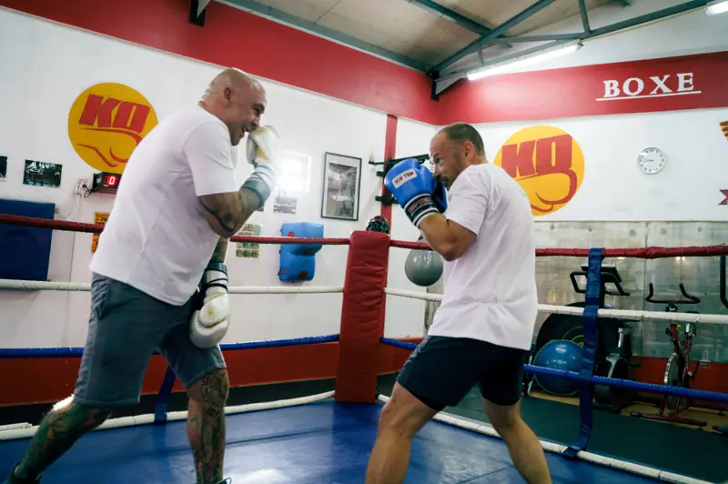 Two participants facing each other during a supervised boxing drill in a gym environment