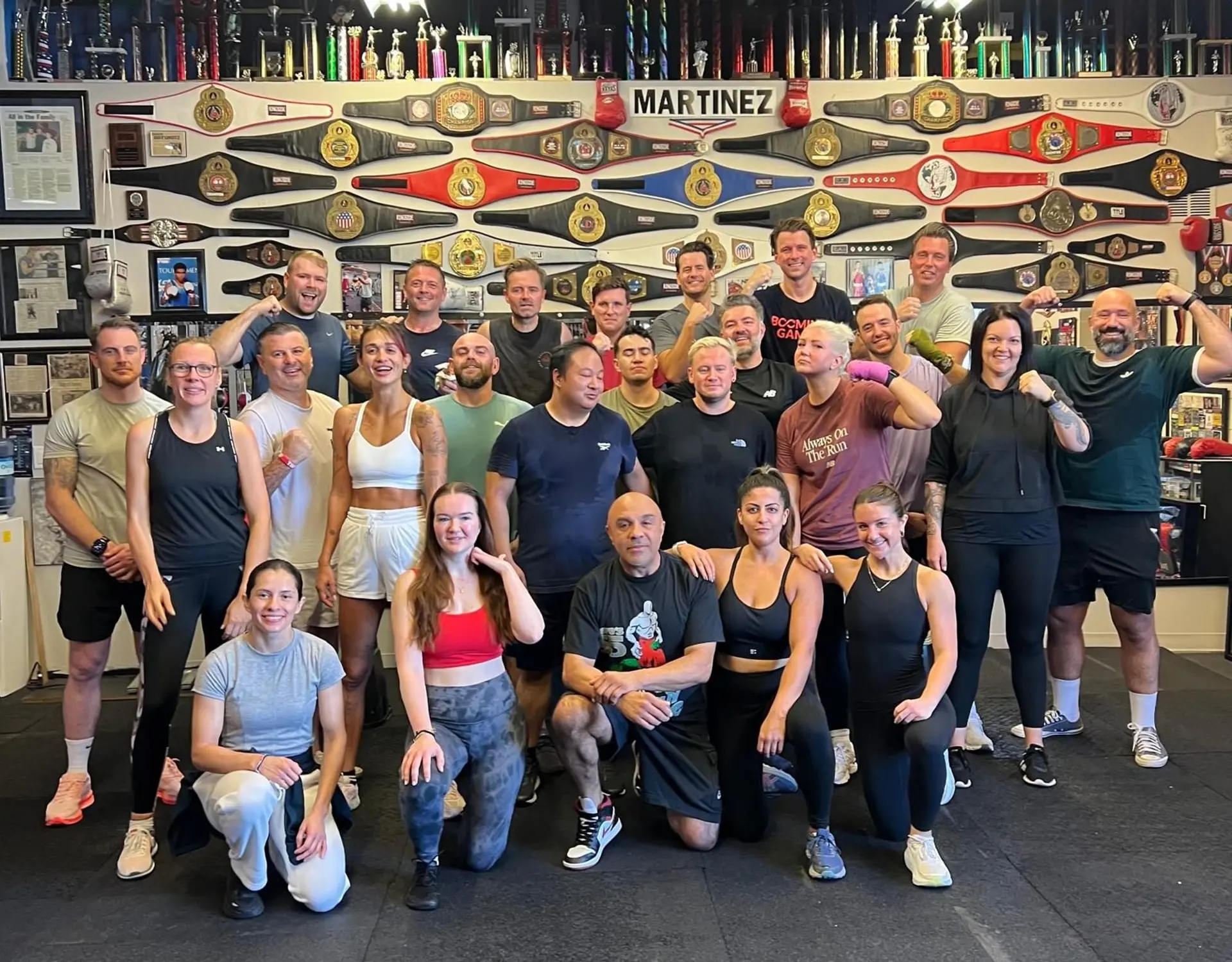 Mixed group of participants posing together inside a boxing gym following a group training session