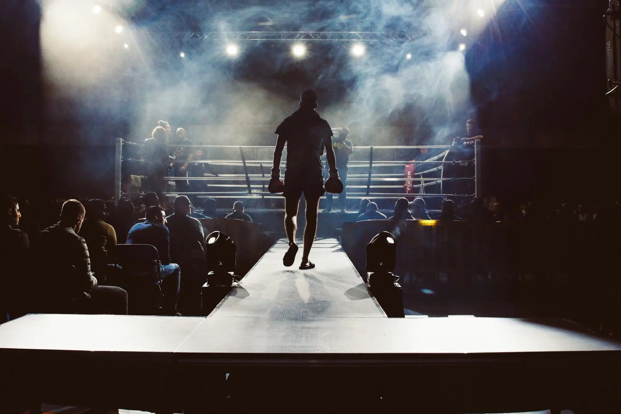 A boxer walks down a smoke-filled runway towards a floodlit ring