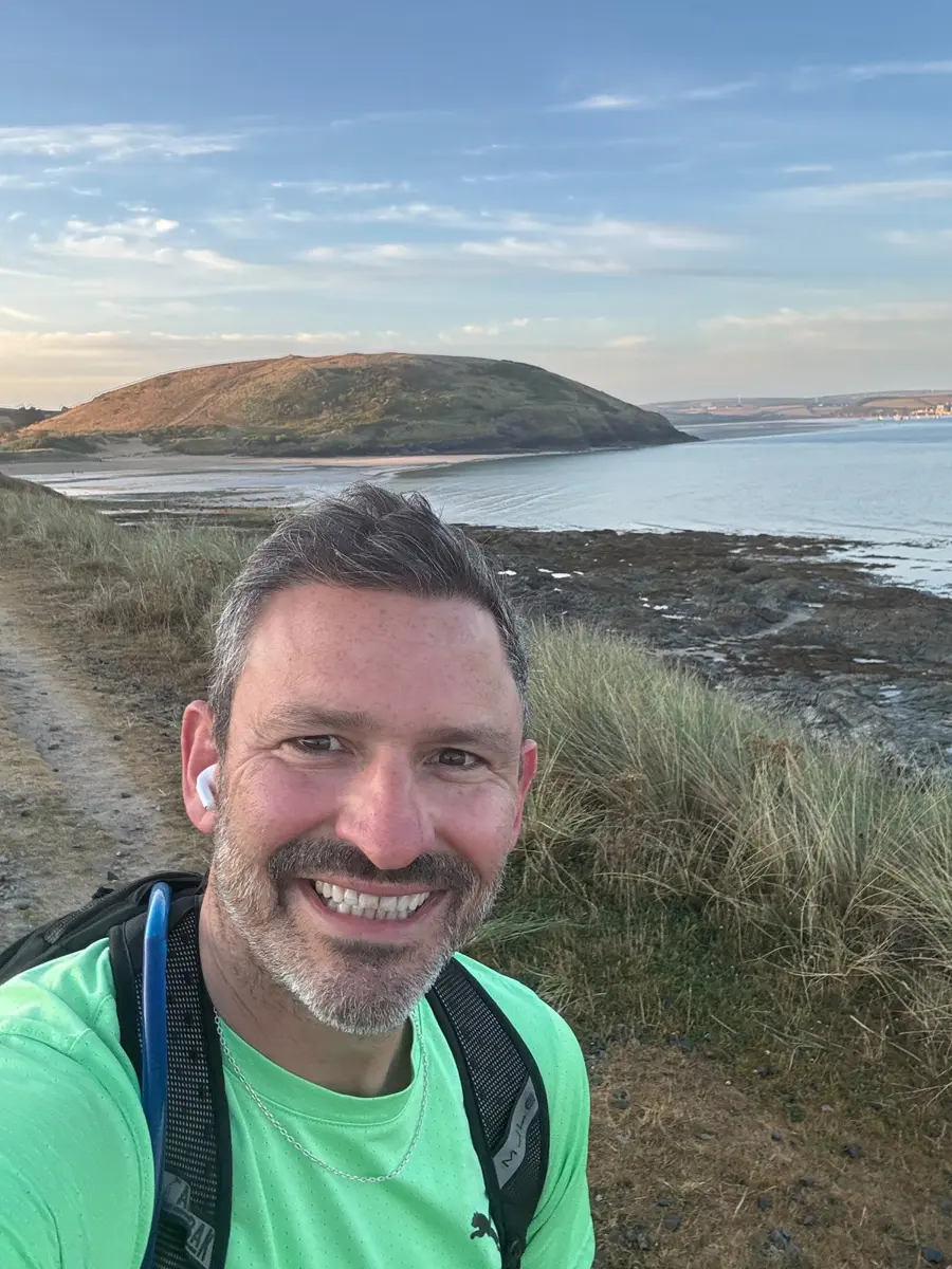 Alex smiling on a coastal path at sunrise